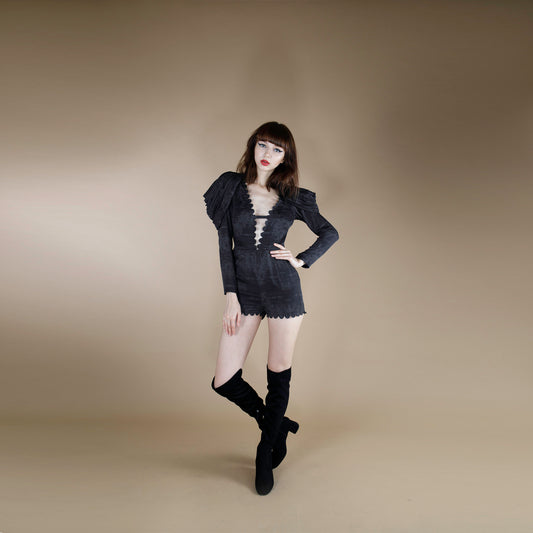 A global small size model wearing a black tonal print short jumpsuit accentuated with cowl cape sleeves. the jumpsuit is made from organic lotus stem silk fabric and adorned with a scallop neck line and hem.  