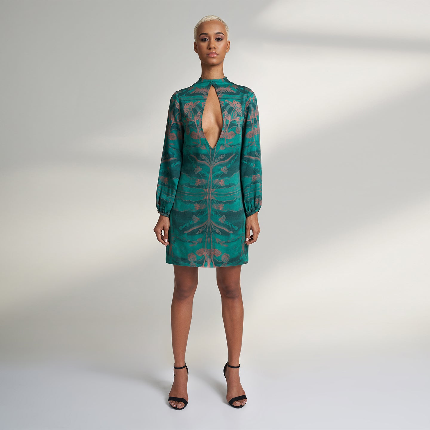 A global small size model wearing a shirt dress printed with hues of green and peach crafted in organic lotus stem silk fabric with a deep front slit neckline and gathered sleeves. the dress is printed with non toxic Gots certified inks. 
