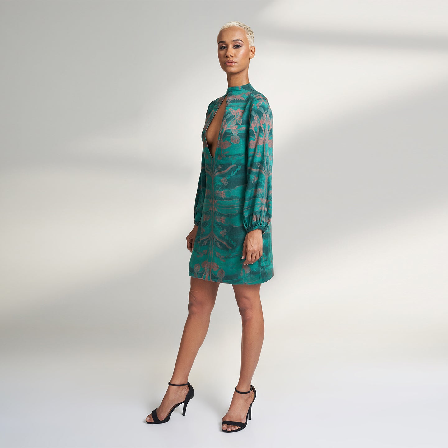 A global small size model wearing a shirt dress printed with hues of green and peach crafted in organic lotus stem silk fabric with a deep front slit neckline and gathered sleeves. the dress is printed with non toxic Gots certified inks. 
