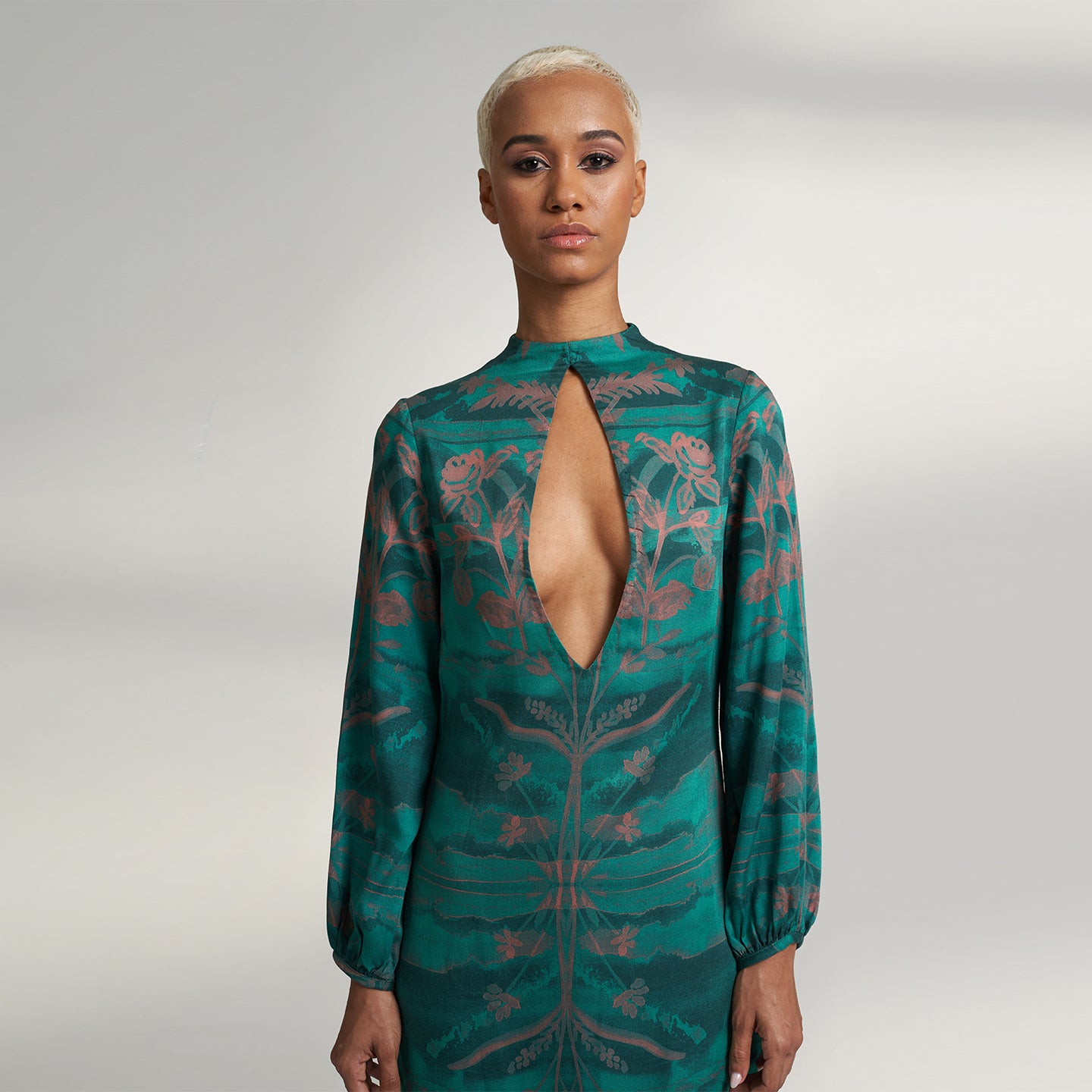 A global small size model wearing a shirt dress printed with hues of green and peach crafted in organic lotus stem silk fabric with a deep front slit neckline and gathered sleeves. the dress is printed with non toxic Gots certified inks. 