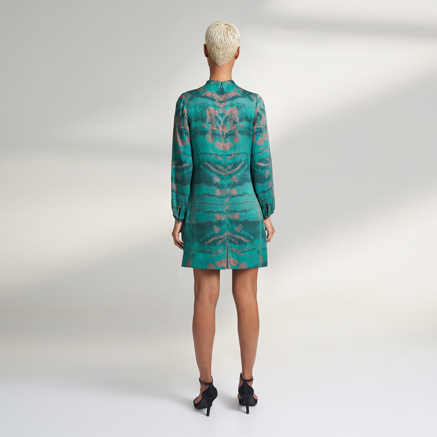 A global small size model wearing a shirt dress printed with hues of green and peach crafted in organic lotus stem silk fabric with a deep front slit neckline and gathered sleeves. the dress is printed with non toxic Gots certified inks. 