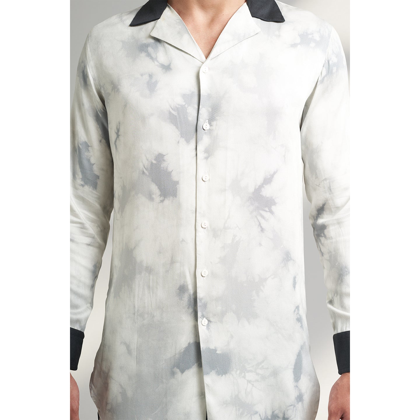 A medium-sized model showcases a Long Printed Cuban Collar shirt in organic Lotus Stem fabric, featuring a solid black collar and cuffs. Paired seamlessly with black trousers made from the same organic lotus stem fabric, presenting a stylish front zoom pose.