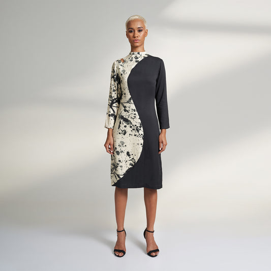 A GLOBAL SMALL SIZE MODEL wearing a black and cream midi dress with one side in solid black and other side in cream with black print on it. the dress is highlighted with a key hole on the right shoulder. 